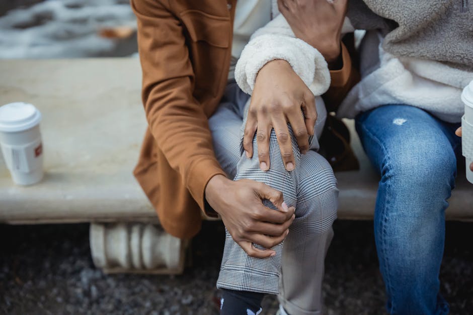 Unrecognizable African American person hugging faceless partner while sitting on bench with takeaway coffee during date on street on blurred background