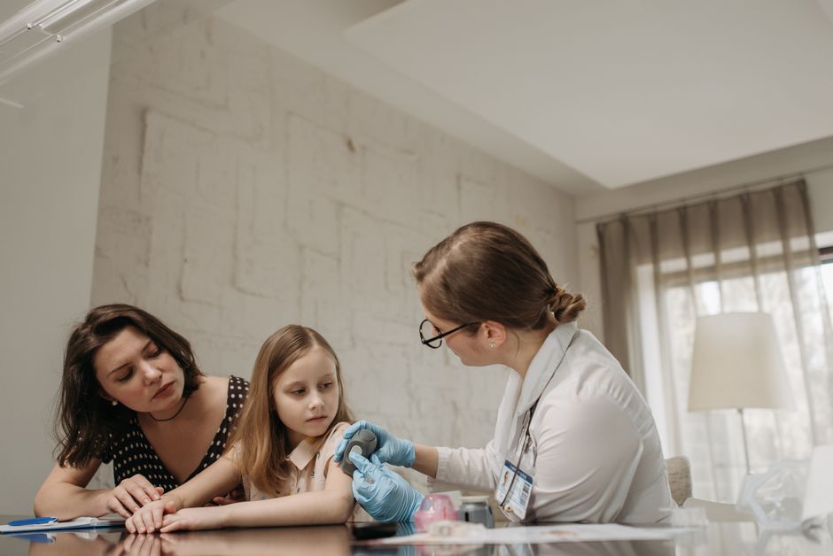 Mother and daughter consult with doctor about child vaccination in a medical office.