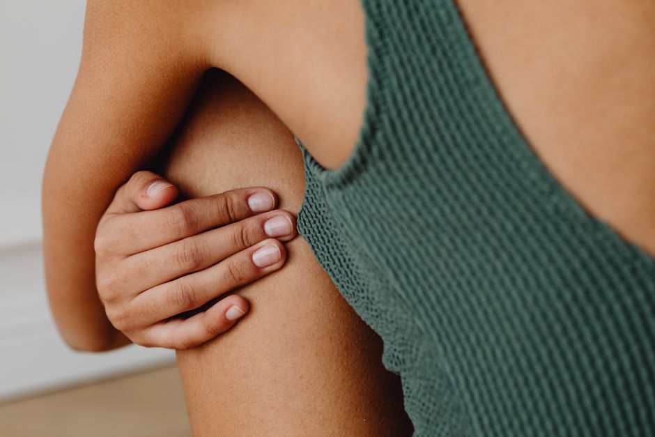 A close-up of a person's hand gently resting on their knee in a minimalist, intimate setting.