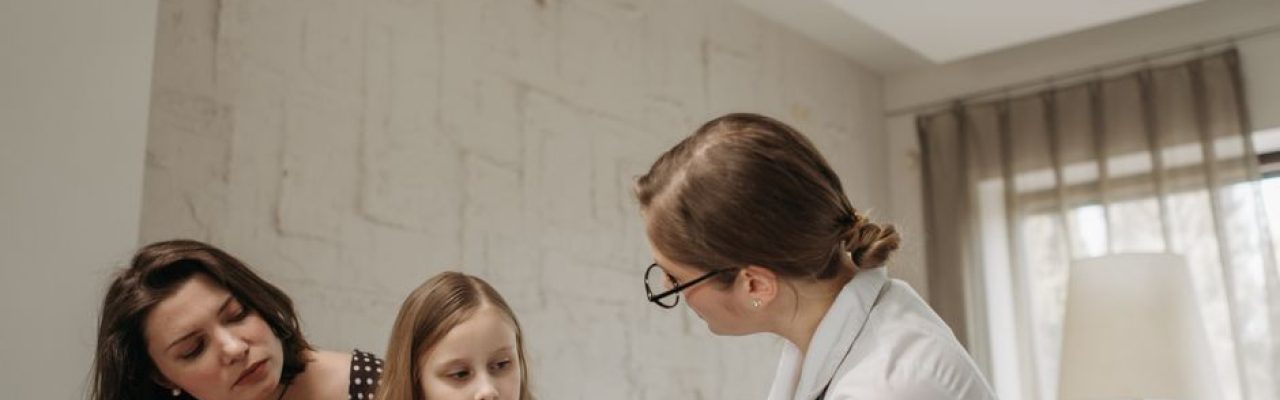Mother and daughter consult with doctor about child vaccination in a medical office.