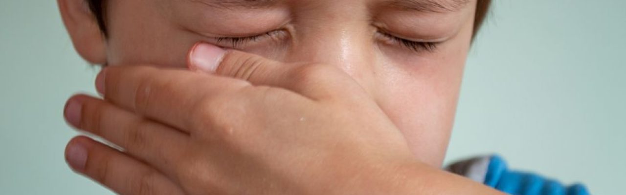 Portrait of crop upset little child with brown hair and closed eyes crying and wiping tears from cheek against white background
