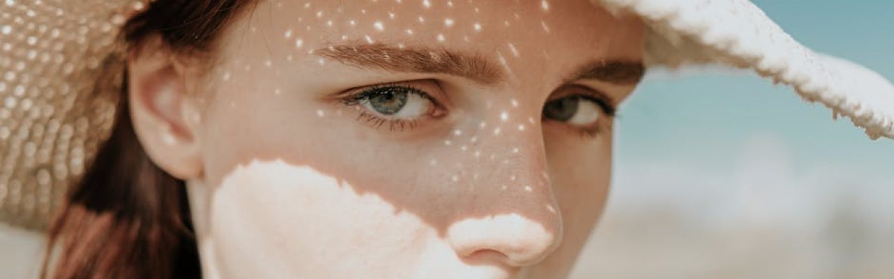 Close-up of a girl in a straw hat with sunlight casting patterned shadows on her face.